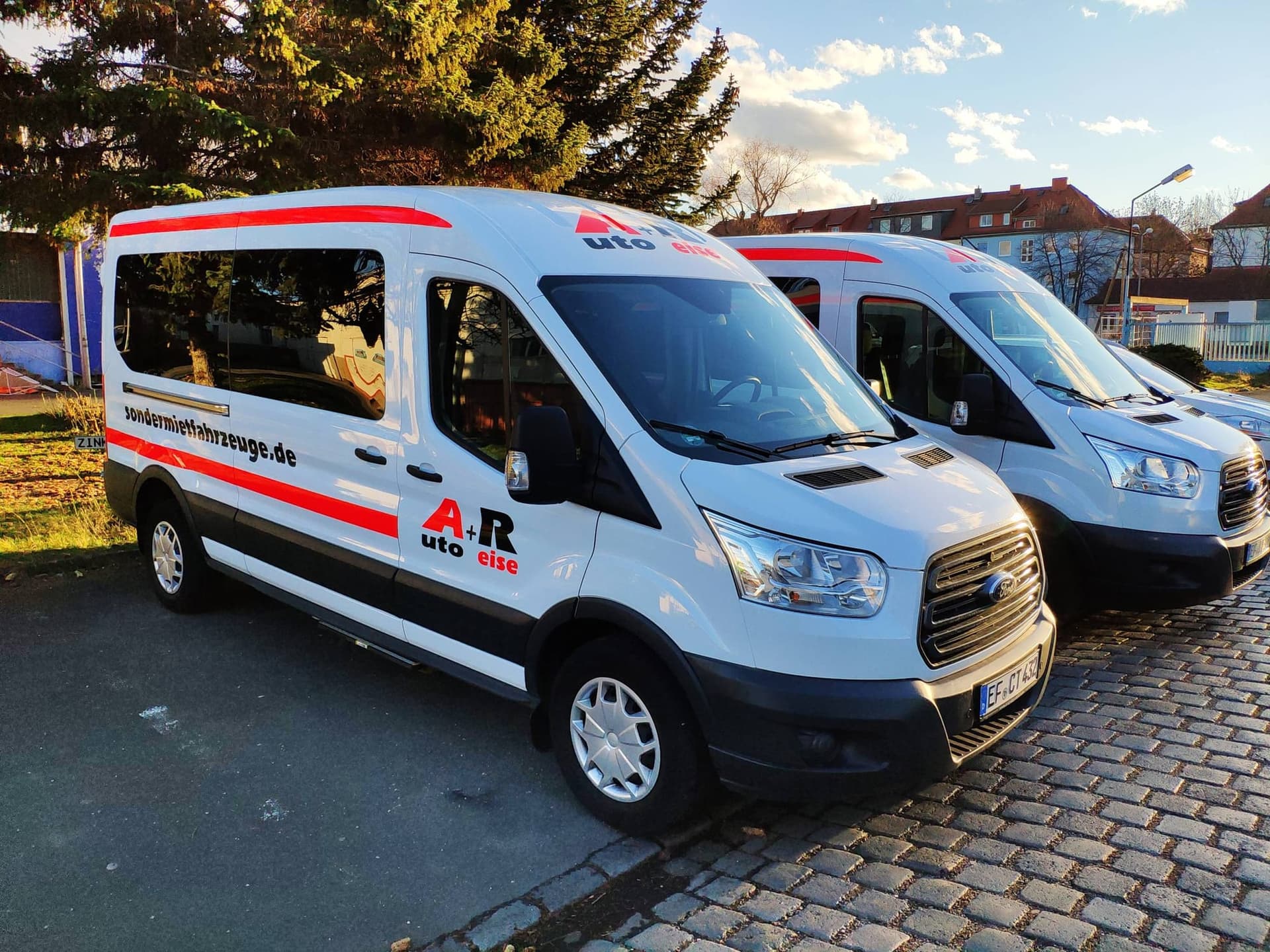 Zwei Ford Transit Kleinbusse in Weiß mit A+R-Beschriftung, vorn der angebotene 9-Sitzer
