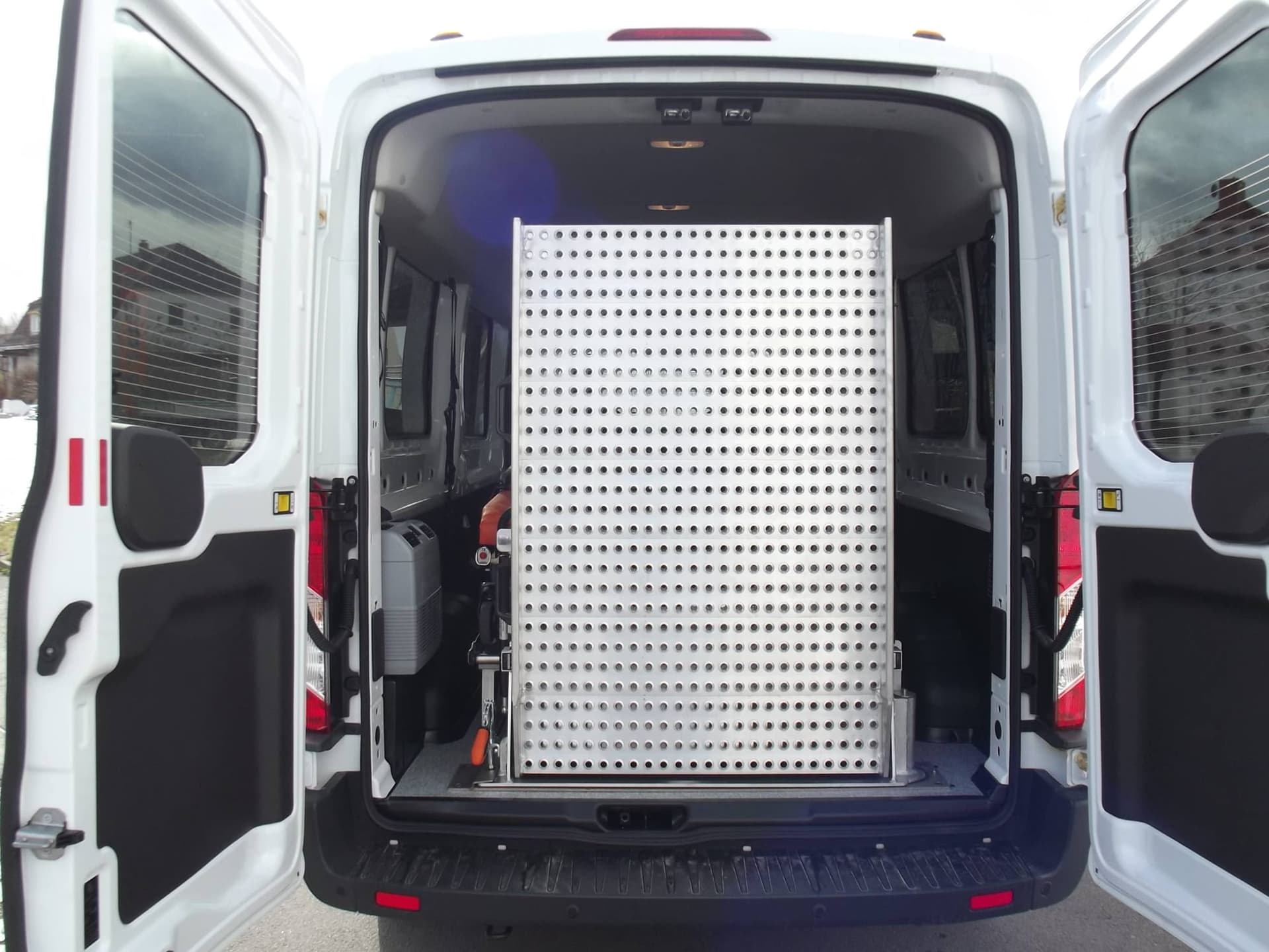 Geöffnete Hecktüren eines Ford Transit, hochgeklappte Auffahrrampe aus gelochtem Aluminium